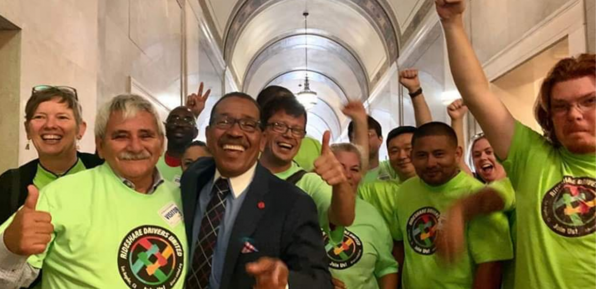 Happy people in neon yellow RDU shirts, plus a man in a suit, raise jubilant fists in a legislative hallway