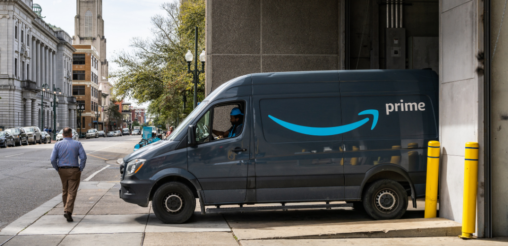 Amazon van exiting a building, about to turn onto a city street, with pedestrian crossing in front
