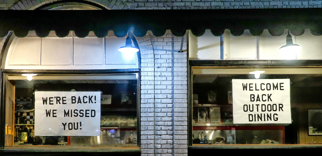 Signs in shop windows: "WE'RE BACK! WE MISSED YOU! WELCOME BACK OUTDOOR DINING"