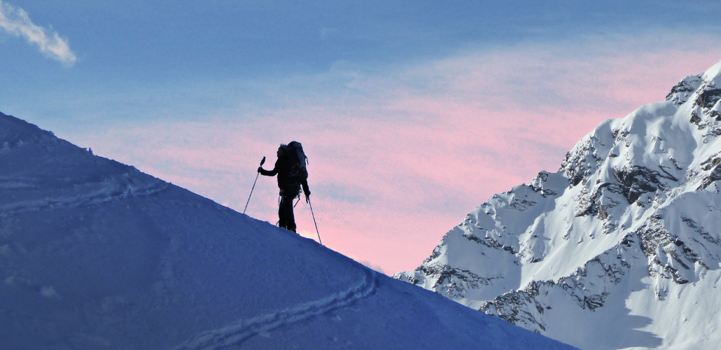 Silhouette of a skier ascending a mountain slope with pink sky in background
