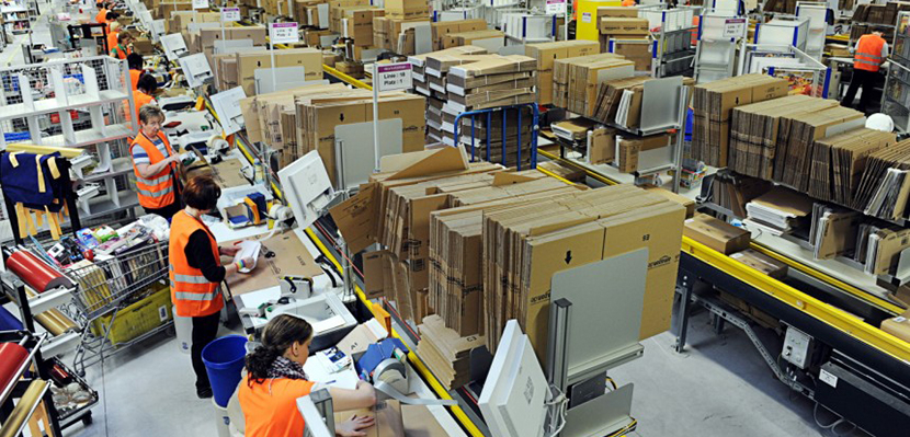 Amazon warehouse with goods on shelves and workers in orange vests working.