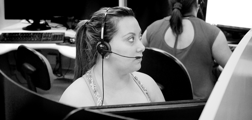 female call center worker with headset at cubicle, other workers in background
