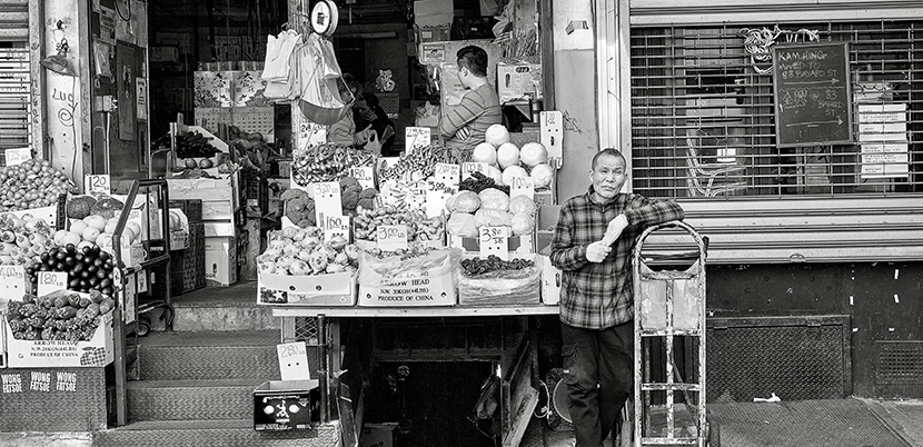 Produce seller with his sidewalk stand in Chinatown, New York, in front of store
