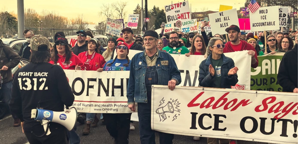 People march in the street carrying various banners and signs. The most visible banners says "Labor says ICE out." Others partially visible are for two Oregon health care unions, OFNHP and ONA. Their red and green shirts (respectively) are also visible, and someone has a blue AFT shirt. Many handmade picket signs are visible, including "We are all Alex," "Unions want ICE out," "Hold ICE accountable," and "Ge(stop)o the bullshit" 