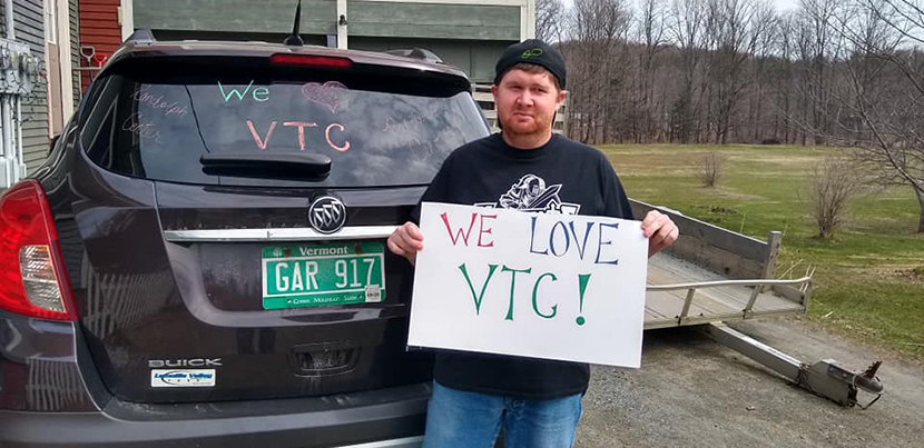 protester for VSCS Thrive! with a sign and his car that has a pro-VTU slogan on the back windshield