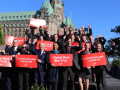 20 flight attendants in uniform hold red signs saying “unpaid work won’t fly” in both French and English 