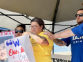 A woman cries while two men in blue Machinists t-shirts comfort her with a hand on her shoulder. Next to her is a woman holding a sign that says “Free Max.”