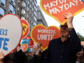 People march with heart-shaped signs saying “workers unite” and “May Day!”