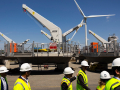 A group of people in hi-viz vests and hardhats walk by huge turbine components