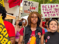 Several people with colorful signs in red and orange face the camera, one says “Delbar treat your workers right”