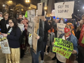 a speaker at a mic set up on the sidewalk is backed up by people holding signs about lead in schools
