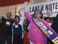 Several people stand on stage with fists raised and with a Labor Notes banner behind them.