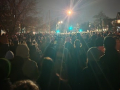 photo taken at night shows a giant crowd of people in a residential street, facing away from the viewer, silhouetted by a streetlight
