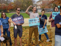A group of excited people hold blue signs saying “Yes on 1”
