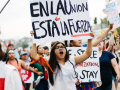 A group marches, one woman holds a sign above her head in Spanish: “En La Union Esta La Fuerza,” with a butterfly on it. Meaning “our strength lies in unity.”