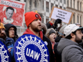A group of 20 protesters with UAW and Save Our Services signs, many are yelling