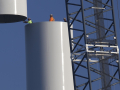 Workers join the top piece of a giant wind turbine to the bottom.  They are tiny against its hugeness.