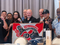 A group of a dozen men of various ages hold a red and white banner that says “Estibadores”