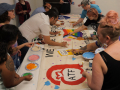 Several people work around a table adding colorful paints to a banner. Photo: ATF