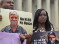 A man and a woman hold signs saying “no NLRB, no voice” with the columns of a government building behind them
