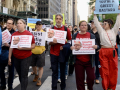 Eight people walk towards the camera, three with signs that say, “shame, Russel Vought”