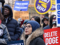 A group of worried-looking protesters hold signs about government cuts