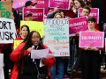 CFPB workers at a rally holding pink signs that say Solidarity and other handmade signs with slogans like CFPB Protects All Consumers.