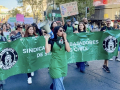 Workers in green aprons march behind a union banner.