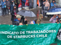 Five workers in the rain hold a green banner that says Chilean Starbucks Union in Spanish