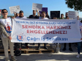 A group of 30 men and women with signs in Turkish stand outside behind a banner